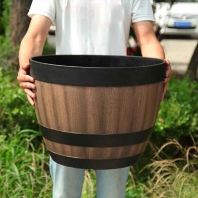 pot de fleur en tonneau imitation bois porté entre les mains d'un jardinier